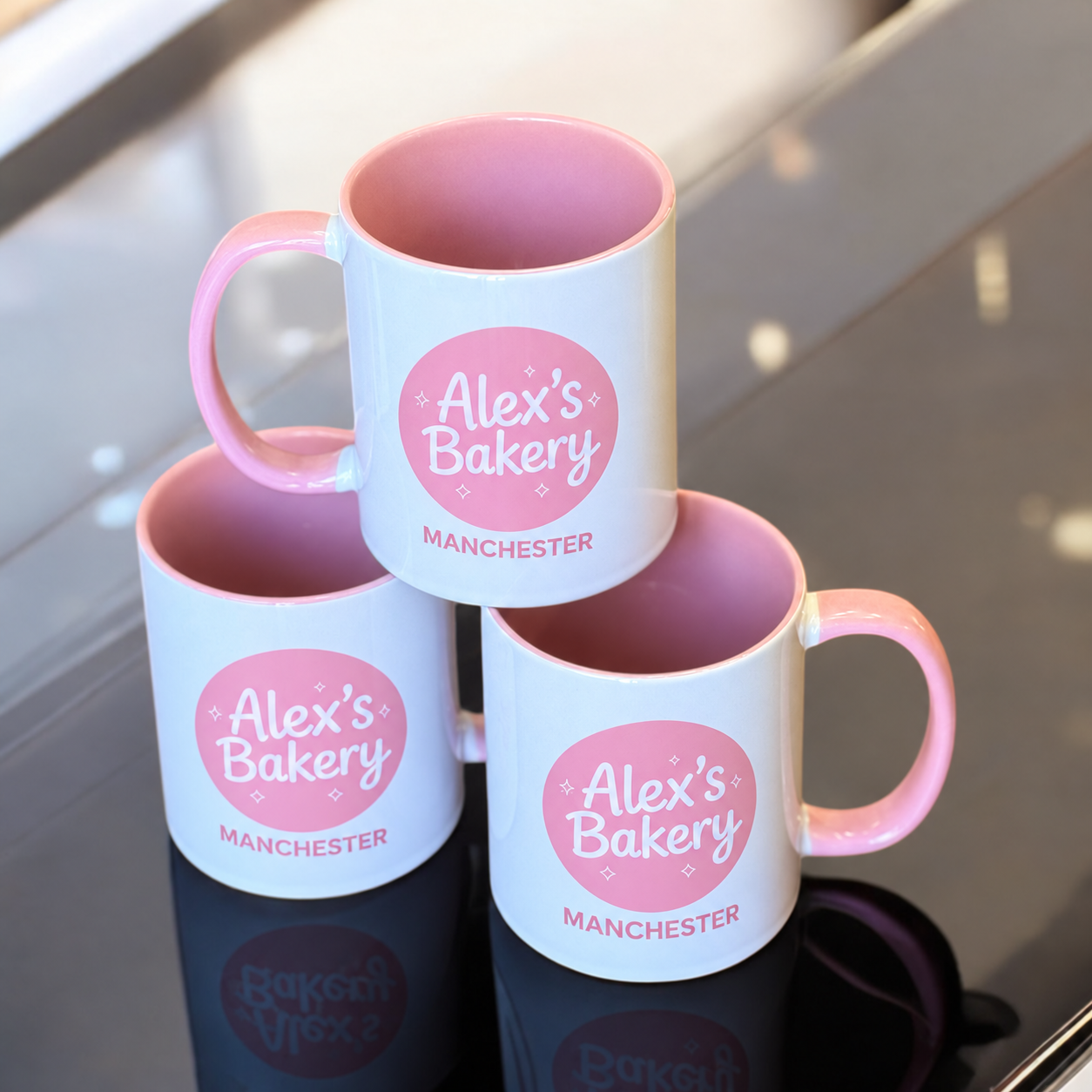 Stack of Alex's Bakery pink branded mugs for gifting